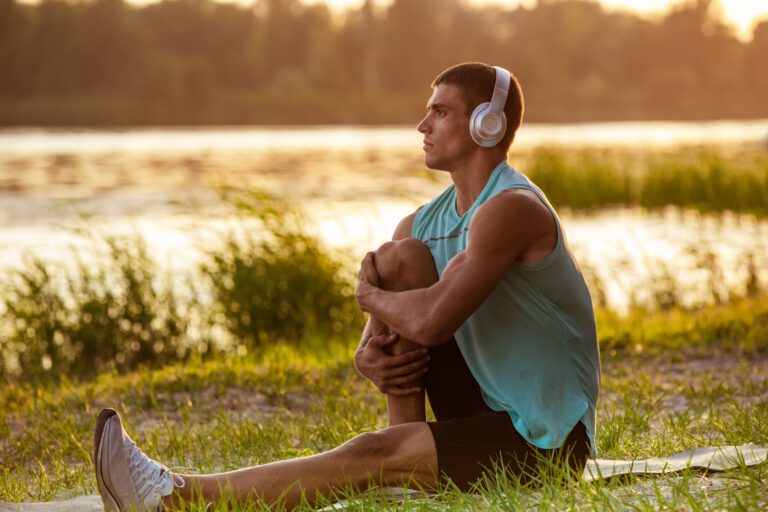 Man sitting cross-legged near a lake, practicing meditation with headphones via the Begin Mindfulness app